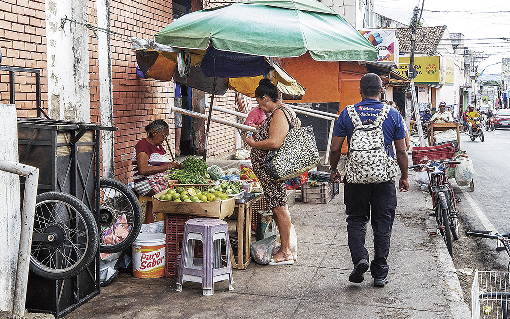 En kvinna handlar i ett marknadsstånd med grönsaker på en trottoar i Brasilien.