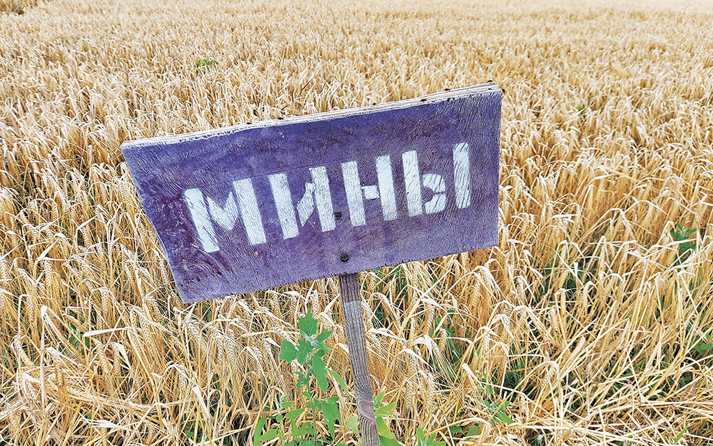 Handmålad skylt som varnar för minor på en sädesåker i Ukraina.