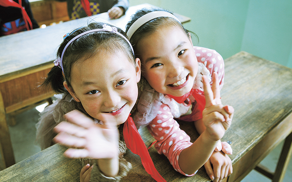 Två unga kinesiska skolflickor tittar in i kameran och ler.