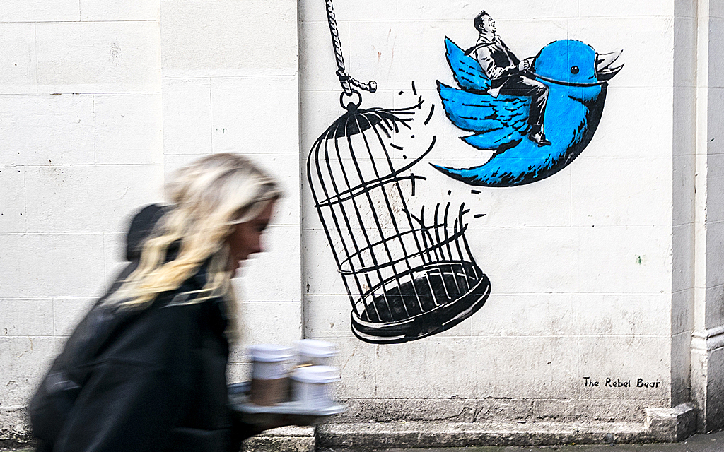 En kvinna passerar förbi en väggmålning föreställande en twitterfågel som flyr ur sin bur med Twitters vd Elon Musk på ryggen