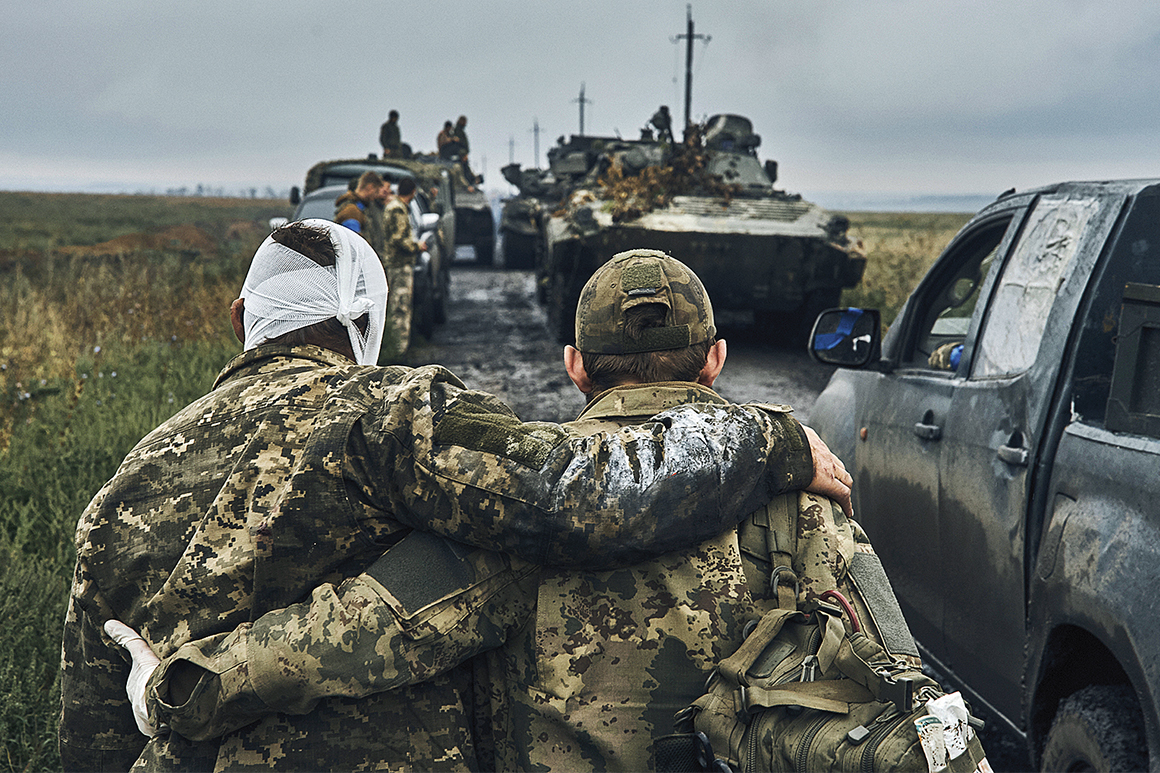 Två ukrainska soldater håller om varandra över ryggen medan de går mot ett stridsfordon på en lerig väg.