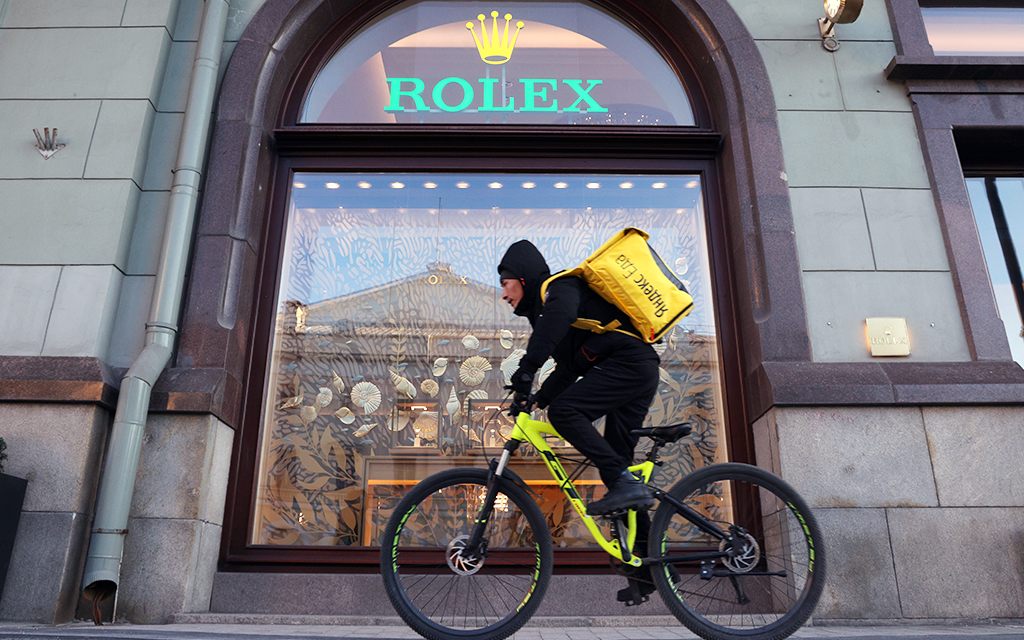 Ett Yandex-cykelbud som är på väg att leverera mat passerar en Rolex-återförsäljare i Moskva.