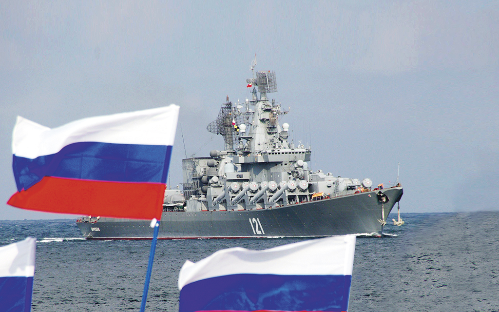 Militärt fartyg med ryska flaggor som vajar i förgrunden.