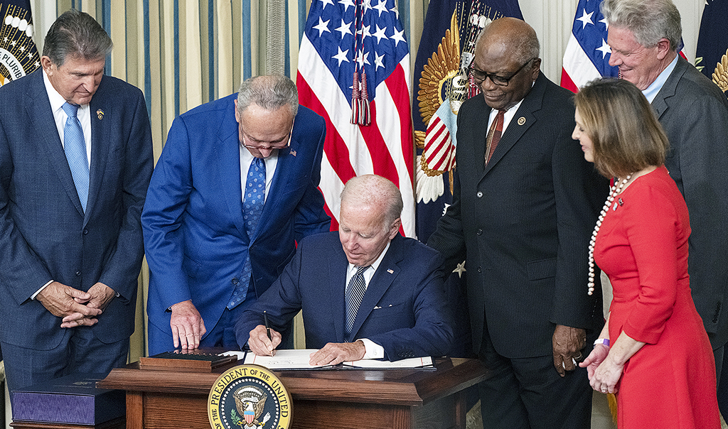 President Joe Biden undertecknar ett papper, omgiven av sina medarbetare.
