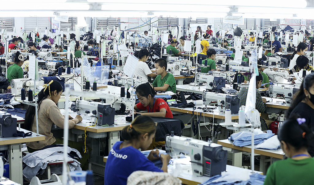 Ett stort antal unga människor sitter och arbetar vid symaskiner i en fabrik i Yangon, Myanmar
