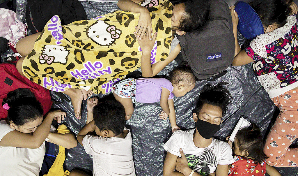 Filippinsk familj ligger och sover på svart plast på marken.