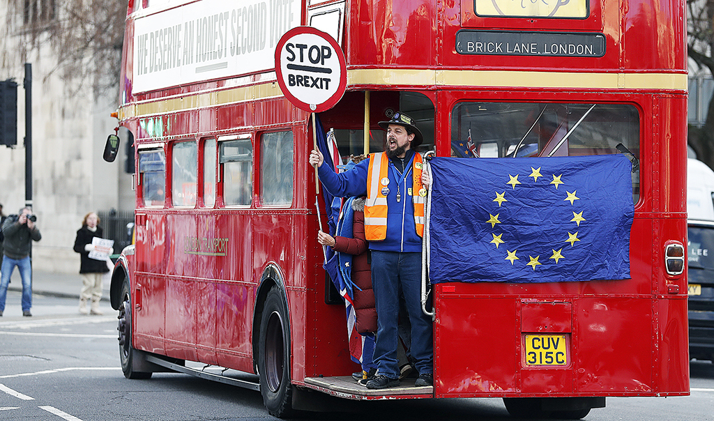 En man står längst bak i en röd buss i London. I sin hand håller han en. stopskylt med texten 