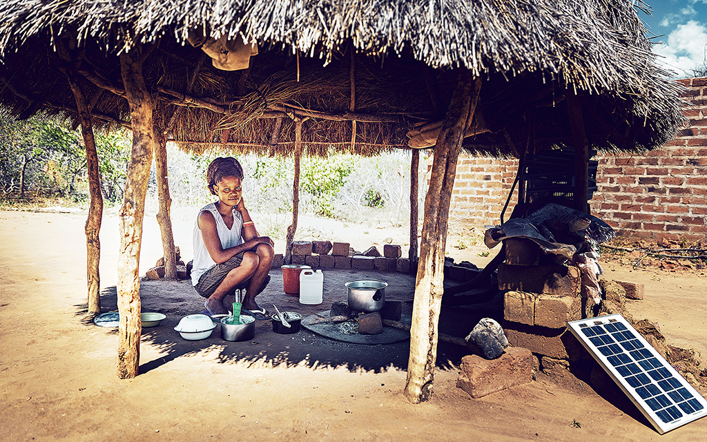 Kvinna i Afrik som sitter under ett grästak ochlagar mat med hjälp av minisollceller.