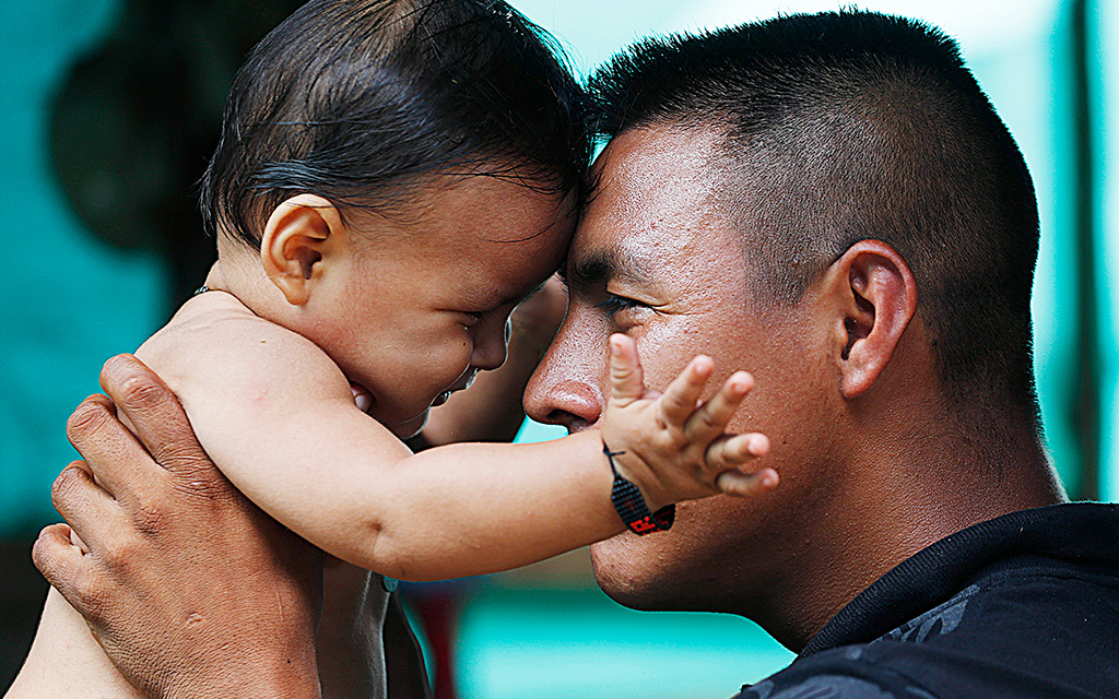 Närbild på en colombiansk pappa som håller upp sin bebis och lutar sin panna mot dennes.