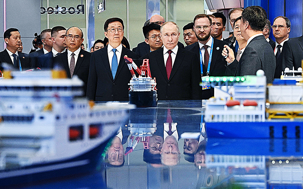 Rysslands president Putin står uppradad tillsammans med ett tjugotal andra män framför en båtmodell på en rysk–kinesisk industrimässa