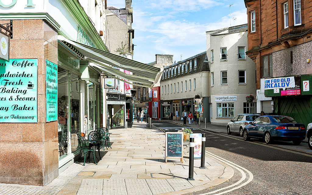Vy över en småstadsgata i byn Kirkcaldy. På båda sidor syns trottoarer men kaféer och små butiker