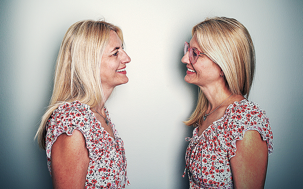 Två kvinnliga tvillingar i likadana blusar står vända mot och tittar på varandra.