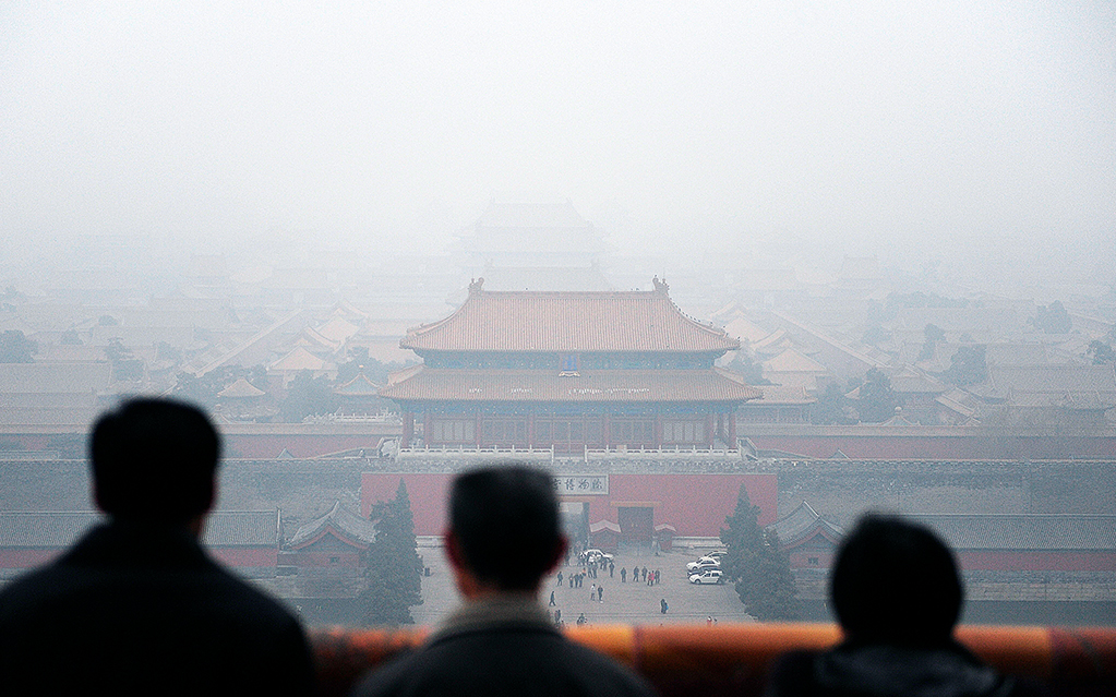 Tre turister blickar ut mot Förbjudna staden i Peking. Året är 2009 och luften är full av smog.