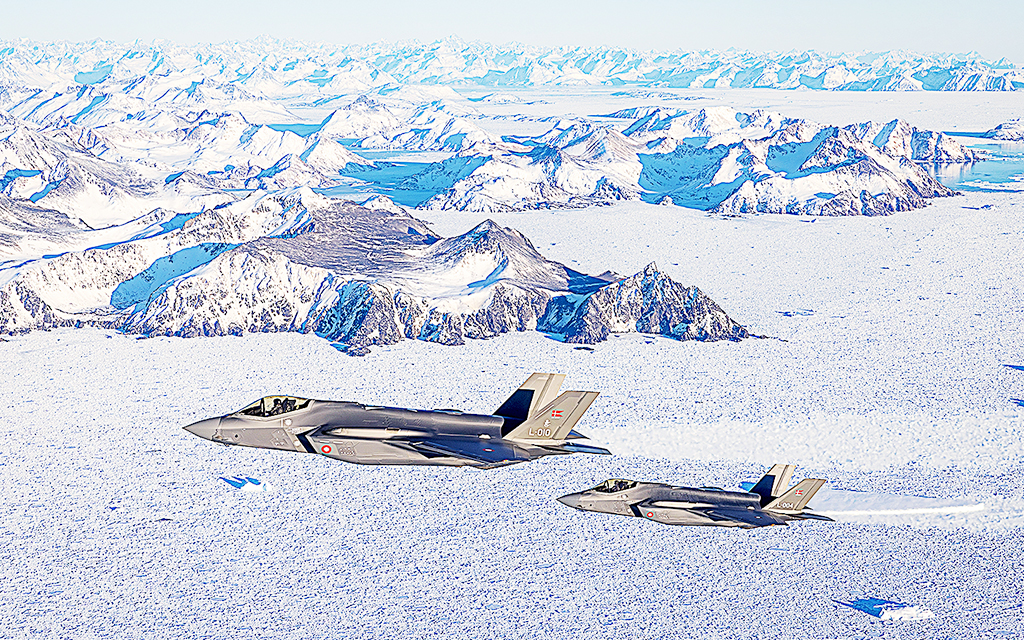 Danska F-35 patrullerar Grönlands östra kust i vintrigt landskap. I bakgrunden syns snöklädda bergstoppar.