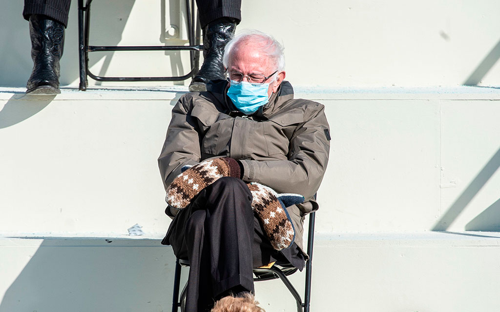 Man i ytterkläder sitter på stol, iklädd ansiktsmask och ser eftertänksam ut.