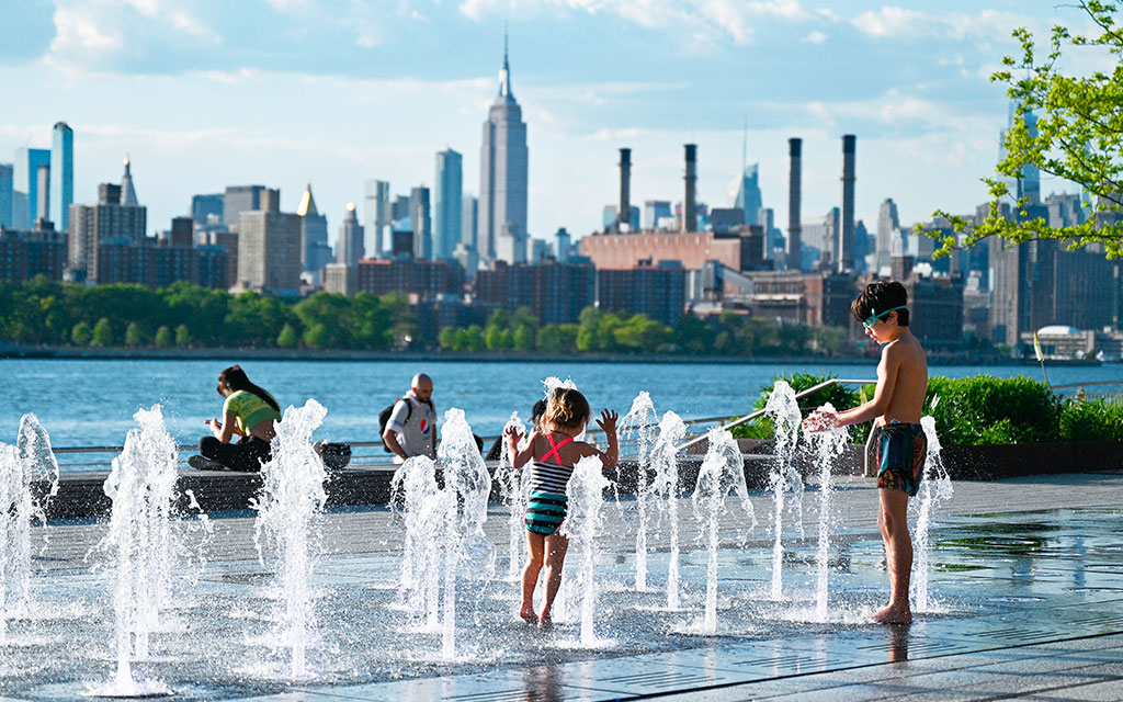 Barn leker i vattenfontäner med New Yorks skyline i bakgrunden.