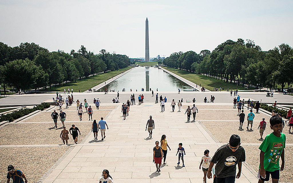 Människor promenerar vid Washingtonmonumentet med spegelblanka vattenytor.